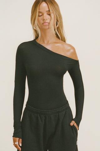 Front view of model posing in the fitted and lighweight black modal Asymmertical Long Sleeve top with an asymmetrical neckline and single-shoulder design