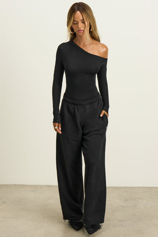 Full body front view of model posing in the fitted and lighweight black modal Asymmertical Long Sleeve top with an asymmetrical neckline and single-shoulder design