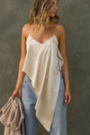 Front view of model posing the flowy champagne Asymmetrical Silk Tank with a V-neckline, asymmetrical hem and an open back with thin, versatile straps that can tie straight or crisscross at the back