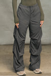 Front view of model from the waist down posing in the relaxed fit, jet nylon Ruched Track Pant with a wide leg, side ruched panels and finished with a drawcord waist, side pockets and adjustable button closures at the ankle.