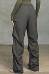 Back view of model from the waist down posing in the relaxed fit, jet nylon Ruched Track Pant with a wide leg, side ruched panels and finished with a drawcord waist, side pockets and adjustable button closures at the ankle.