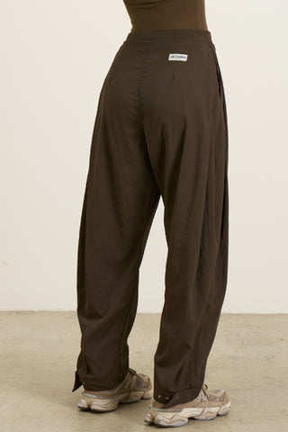 Back view of model from the waist down posing in the oversized, horseshoe-style espresso nylon Barrel Pant with side pockets, zip fly, pleated sides and adjustable snap closures at the ankle.