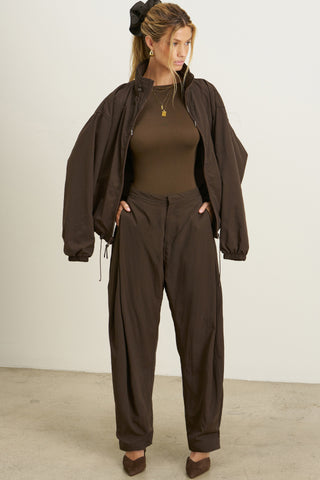 Full body front view of model posing in the oversized, horseshoe-style espresso nylon Barrel Pant with side pockets, zip fly, pleated sides and adjustable snap closures at the ankle.