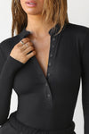 Close up detail front view of model posing in the fitted and stretchy black rib Button Down Henley long sleeve top with a high crew neckline and front buttons that reach about halfway down the shirt