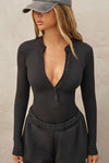 Front view of model posing in the fitted and stretchy black rib Button Down Henley long sleeve top with a high crew neckline and front buttons that reach about halfway down the shirt