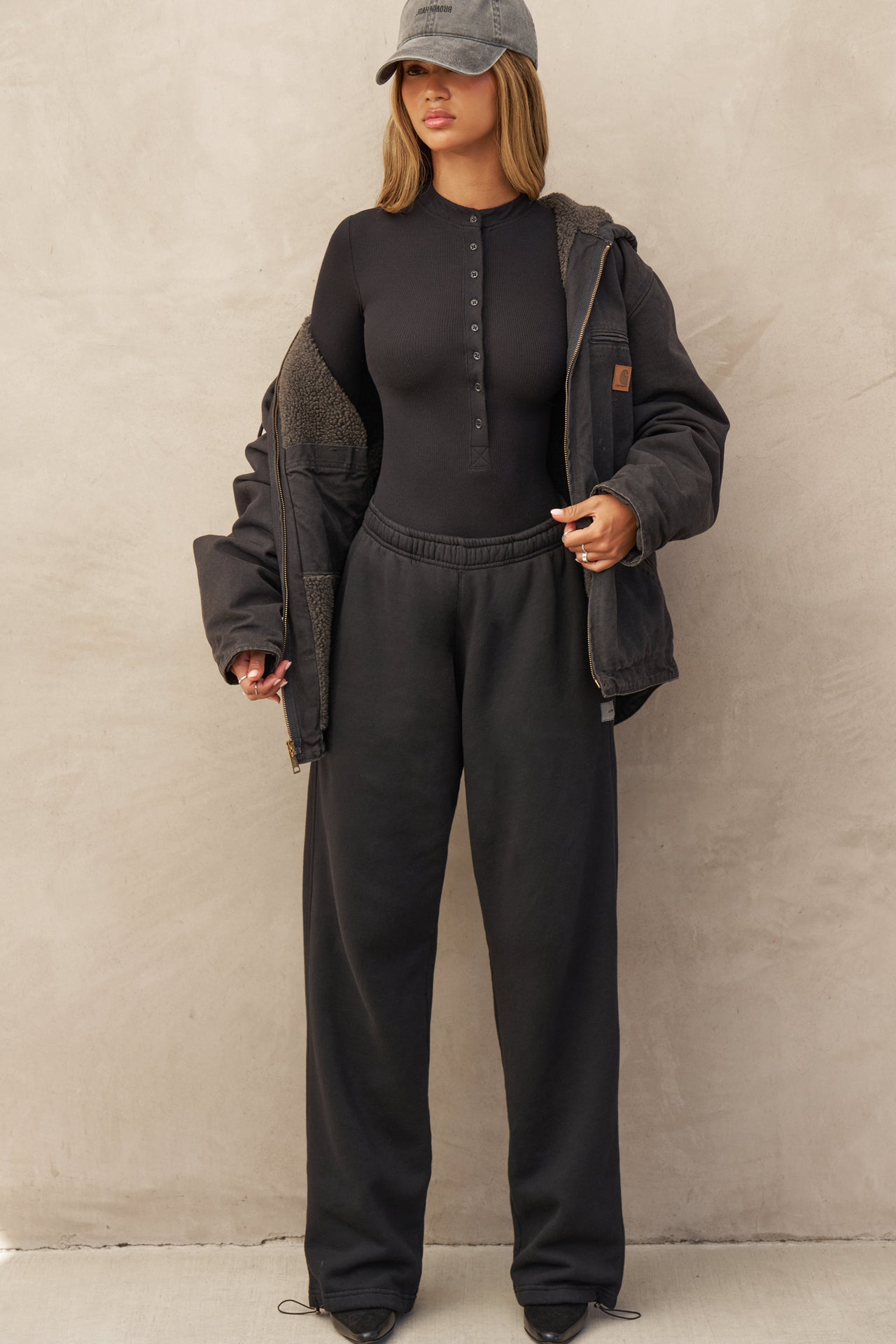 Full body front view of model posing in the fitted and stretchy black rib Button Down Henley long sleeve top with a high crew neckline and front buttons that reach about halfway down the shirt