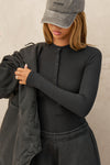 Front view of model posing in the fitted and stretchy black rib Button Down Henley long sleeve top with a high crew neckline and front buttons that reach about halfway down the shirt