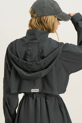Back view of model posing in the jet nylon City Trench coat with oversized silhouette, structured collar, attached hood, self-tie belt and adjustable sweep