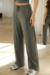 Side view of model from the waist down posing in the relaxed fit spruce modal Relaxed Straight Leg Pant with a wide leg, elastic waistband, adjustable drawstring tie and subtle pleating at the sides.