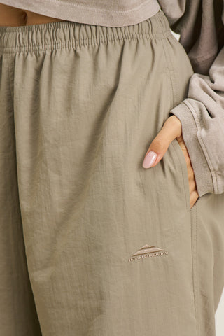 Close up detail side view of model from the waist down posing in the relaxed fit desert sage nylon Classic Track Pant with a straight-leg silhouette, adjustable drawstring elastic waistband and side pockets 