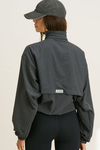 Back view of model posing in the relaxed-fit jet nylon Classic Windbreaker Jacket with a padded collared neck for structure & adjustable corded details at the sweep for cinching