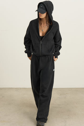 Full body front view of model posing outside in the relaxed fit black french terry Classic Zip Hoodie with a full length front zip closure, side pockets and thumbholes in the fitted cuffs