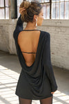 Back view model posing in the relaxed fit black modal Cowl Back Long Sleeve Mini Dress \with a crew neckline, A-line silhouette, adjustable straps at the center back and neck and an open back with a draped cowl detail.