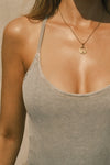 Close up detail front view of model posing in the fitted dune washed rib Cross Back Cami with a scoop neckline and thin adjustable straps that criss cross in the back