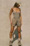 Full body front view of model posing in the fitted dune washed rib Cross Back Cami with a scoop neckline and thin adjustable straps that criss cross in the back
