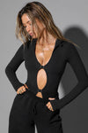 Front view of model posing in the fitted sueded onyx Cut Out Long Sleeve Top with front cutout details, three front adjustable clasps and thumbholes in the sleeve cuffs