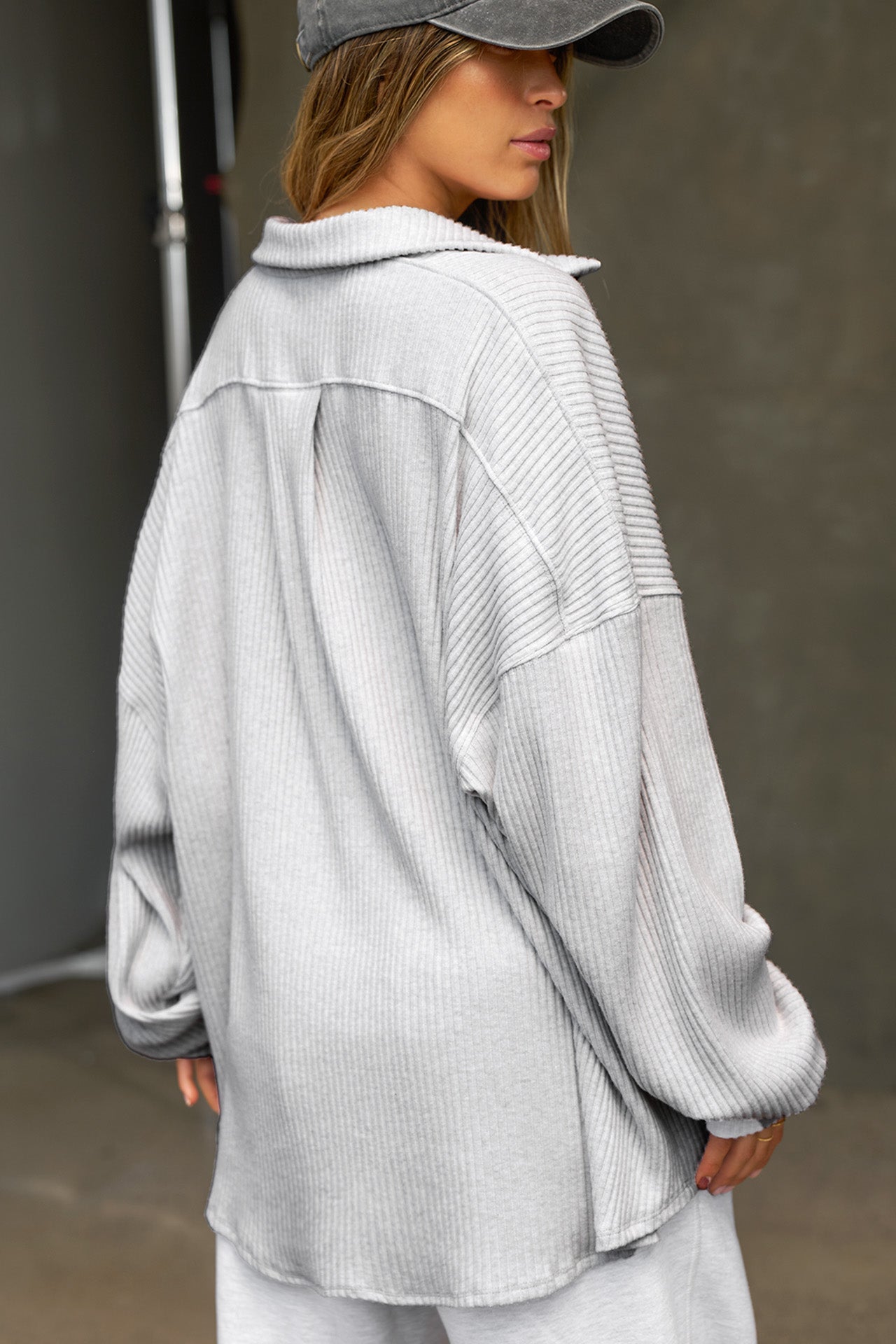 Back view of model posing in the oversized pearl grey luxe knit Deep V Pullover with a plunging collared neckline, dropped shoulders and back panel details