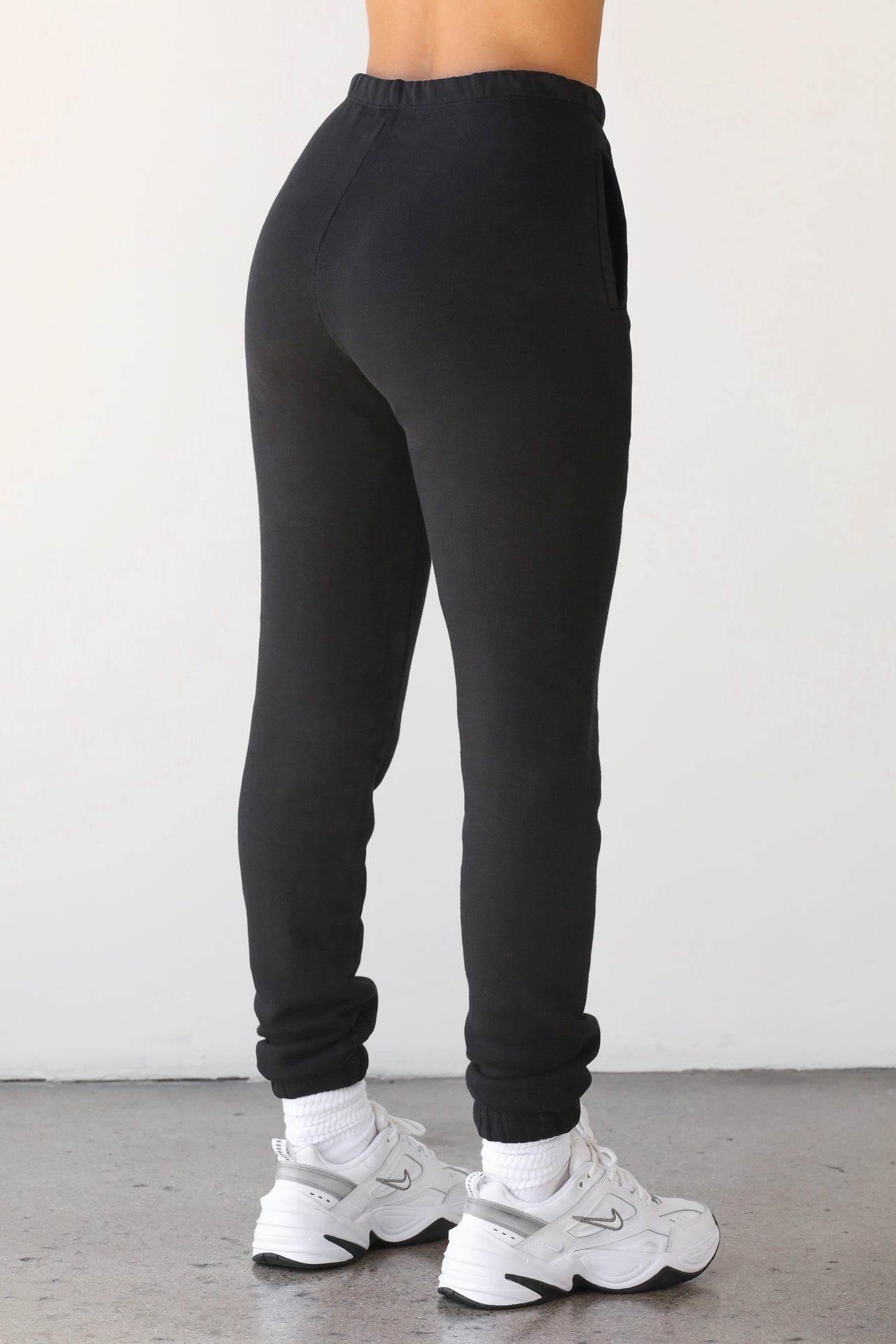 Back view of model from the waist down posing in the tapered black french terry Empire Jogger with side pockets and an elastic waistband and ankle cuffs