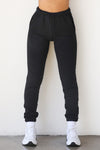 Front view of model from the waist down posing in the tapered black french terry Empire Jogger with side pockets and an elastic waistband and ankle cuffs
