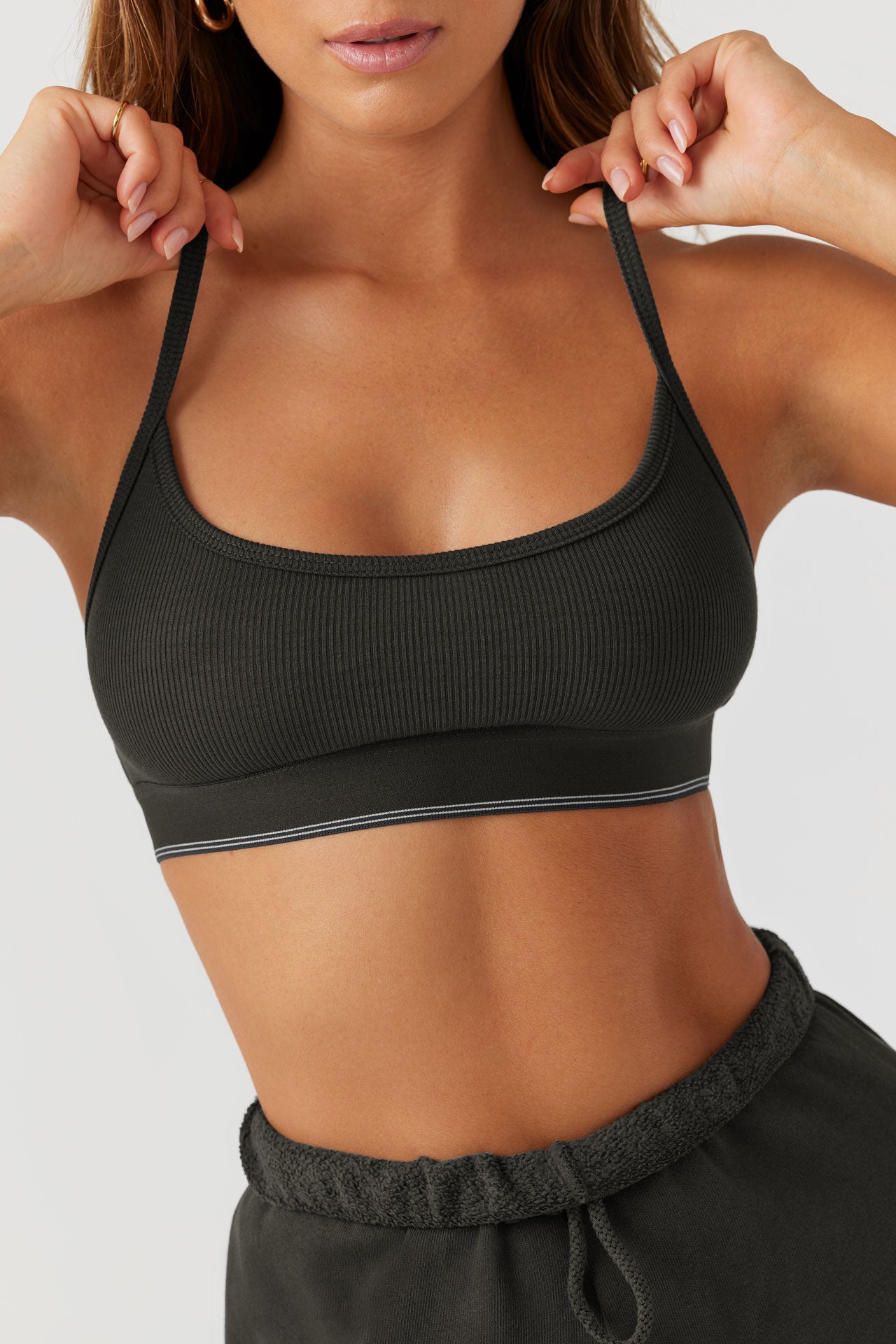 Close up front view of model posing in the fitted and stretchy vintage black flexrib Essential Bra with a scoop neckline, thin straps and an elastic underband printed with two thin horizontal stripes on the bottom