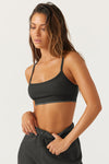 Front view of model posing in the fitted and stretchy vintage black flexrib Essential Bra with a scoop neckline, thin straps and an elastic underband printed with two thin horizontal stripes on the bottom