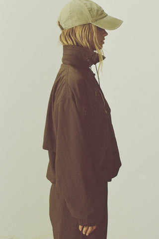 Side view of model posing in the relaxed fit espresso nylon 3/4 Zip Windbreaker jacket with a structured collar and 3/4 zip neckline