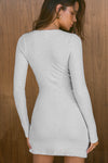Back view of model posing in the soft and fitted pearl grey luxe knit Asymmetrical Button Mini Dress with long sleeves,  a v-neckline and asymmetrical button-front details. 