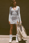 Full body front view of model posing in the soft and fitted pearl grey luxe knit Asymmetrical Button Mini Dress with long sleeves,  a v-neckline and asymmetrical button-front details. 