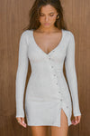 Front view of model posing in the soft and fitted pearl grey luxe knit Asymmetrical Button Mini Dress with long sleeves,  a v-neckline and asymmetrical button-front details. 