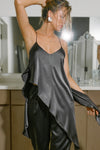 Front view of model posing the flowy iron Asymmetrical Silk Tank with a V-neckline, asymmetrical hem and an open back with thin, versatile straps that can tie straight or crisscross at the back