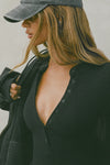 Close up detail front view of model posing in the fitted and stretchy black rib Button Down Henley long sleeve top with a high crew neckline and front buttons that reach about halfway down the shirt