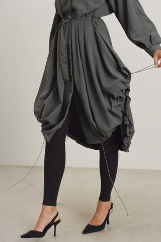 Front view of model from the waist down posing in the jet nylon City Trench coat with oversized silhouette, structured collar, attached hood, self-tie belt and adjustable sweep