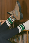Close up detail side view of model adjusting the crew style ribbed soft forest green Classic Stripe Sock