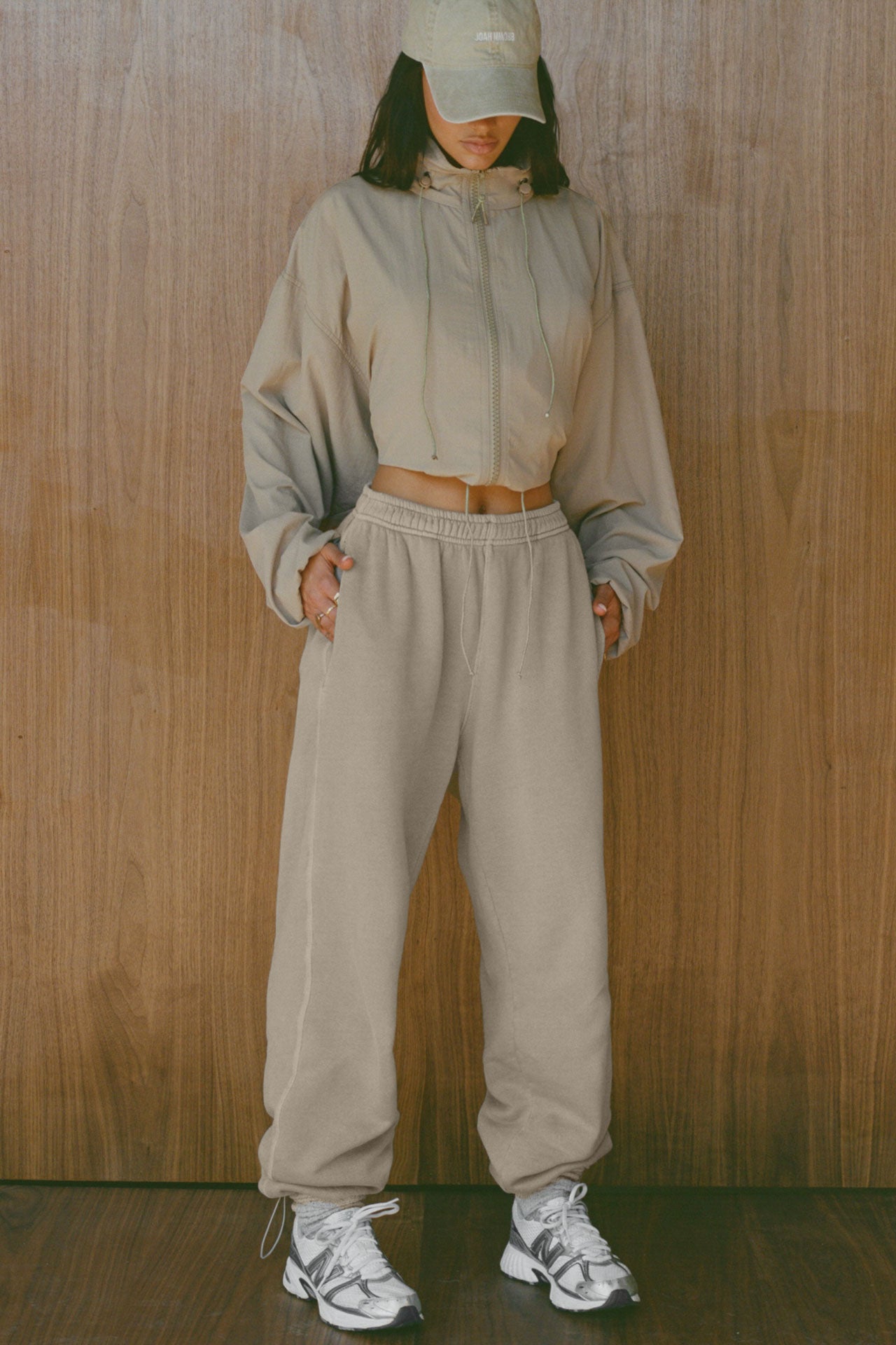 Full body front view of model posing in the oversized desert sage nylon Classic Windbreaker Jacket with a collar, zip-away hood and reflective corded details at the hem, sleeves and neck for cinching.