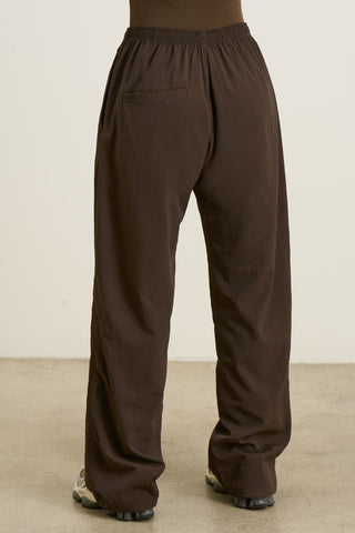 Back view of model from the waist down posing in the relaxed fit espresso nylon Classic Track Pant with a straight-leg silhouette, adjustable drawstring elastic waistband and side pockets 