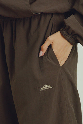 Close up detail side view of model from the waist down posing in the relaxed fit espresso nylon Classic Track Pant with a straight-leg silhouette, adjustable drawstring elastic waistband and side pockets 