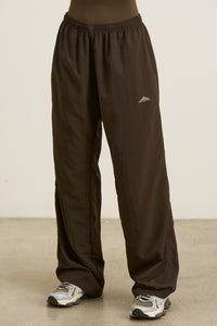 Front view of model from the waist down posing in the relaxed fit espresso nylon Classic Track Pant with a straight-leg silhouette, adjustable drawstring elastic waistband and side pockets 