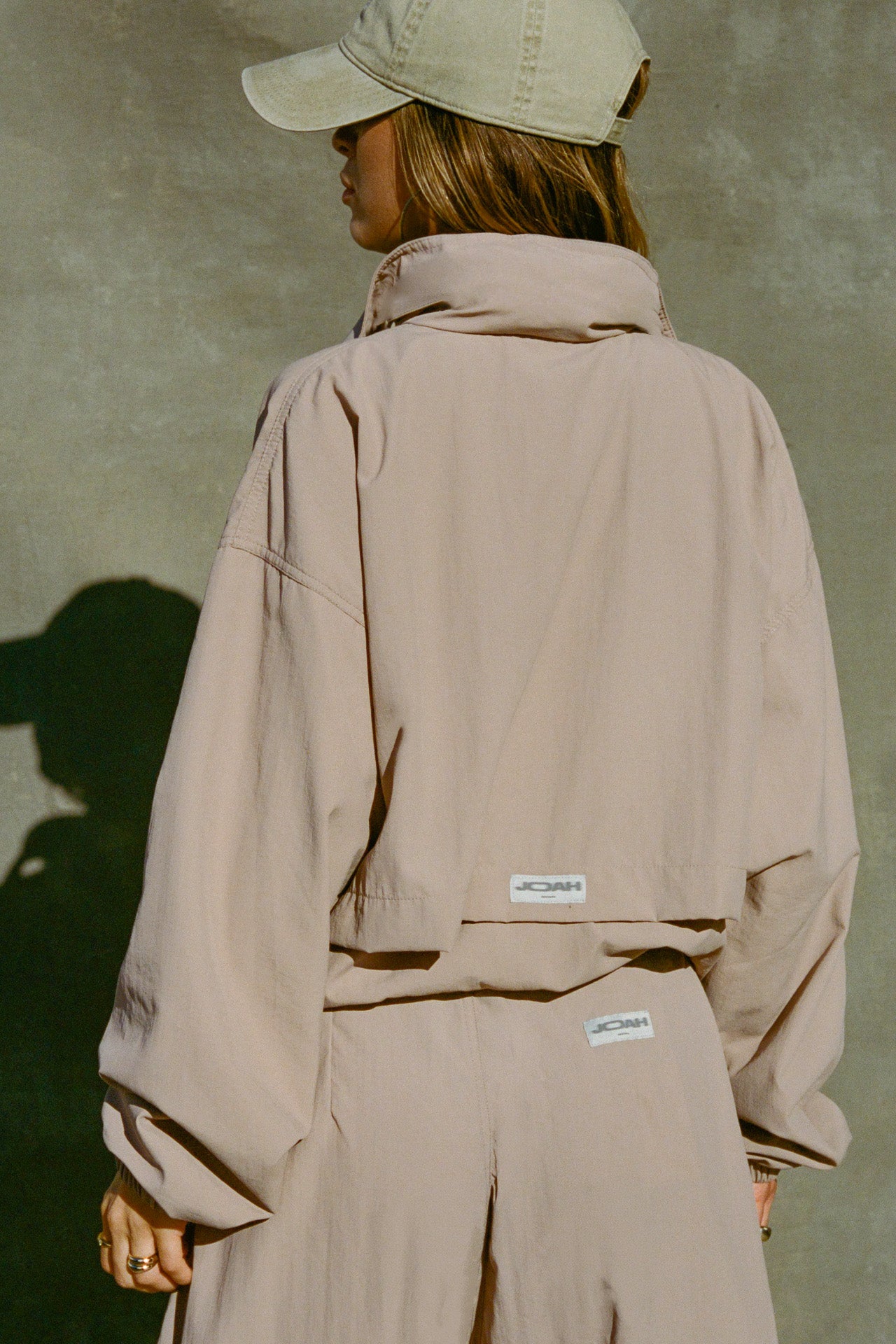 Back view of model posing in the relaxed-fit fawn Classic Windbreaker Jacket with a padded collared neck for structure & adjustable corded details at the sweep for cinching