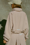 Back view of model posing in the relaxed-fit fawn Classic Windbreaker Jacket with a padded collared neck for structure & adjustable corded details at the sweep for cinching