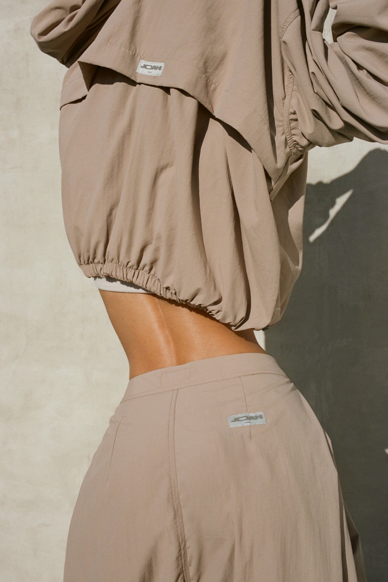 Back view of model posing in the relaxed-fit fawn Classic Windbreaker Jacket with a padded collared neck for structure & adjustable corded details at the sweep for cinching