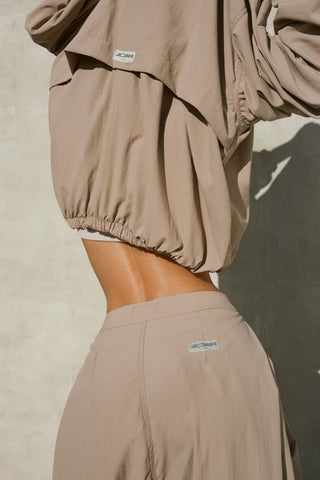 Back view of model posing in the relaxed-fit fawn Classic Windbreaker Jacket with a padded collared neck for structure & adjustable corded details at the sweep for cinching