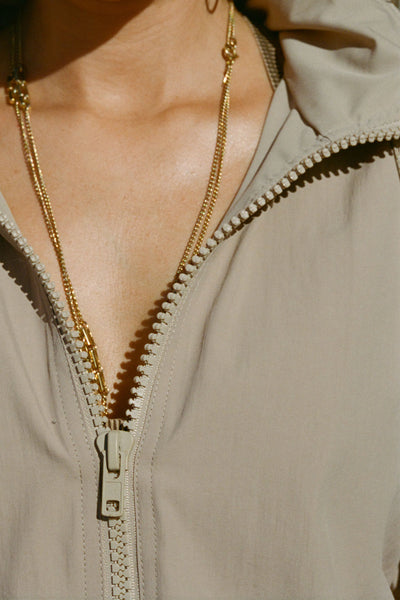 Close up detail view of the front of oversized desert sage nylon Classic Windbreaker Jacket with a collar, zip-away hood and reflective corded details at the hem, sleeves and neck for cinching.