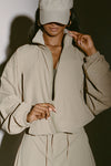 Front view of model posing in the oversized desert sage nylon Classic Windbreaker Jacket with a collar, zip-away hood and reflective corded details at the hem, sleeves and neck for cinching.