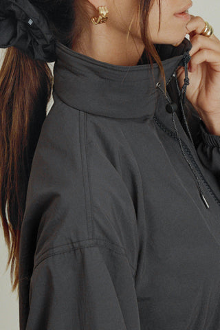 Close up detail side view of model posing in the relaxed-fit jet nylon Classic Windbreaker Jacket with a padded collared neck for structure & adjustable corded details at the sweep for cinching