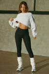 Full body front view of model posing in the loose fit cropped pearl grey french terry Cut Off Sweatshirt with oversized long sleeves, a raw cut hem and a white patch with a black joah brown logo on it sewn on the upper left chest