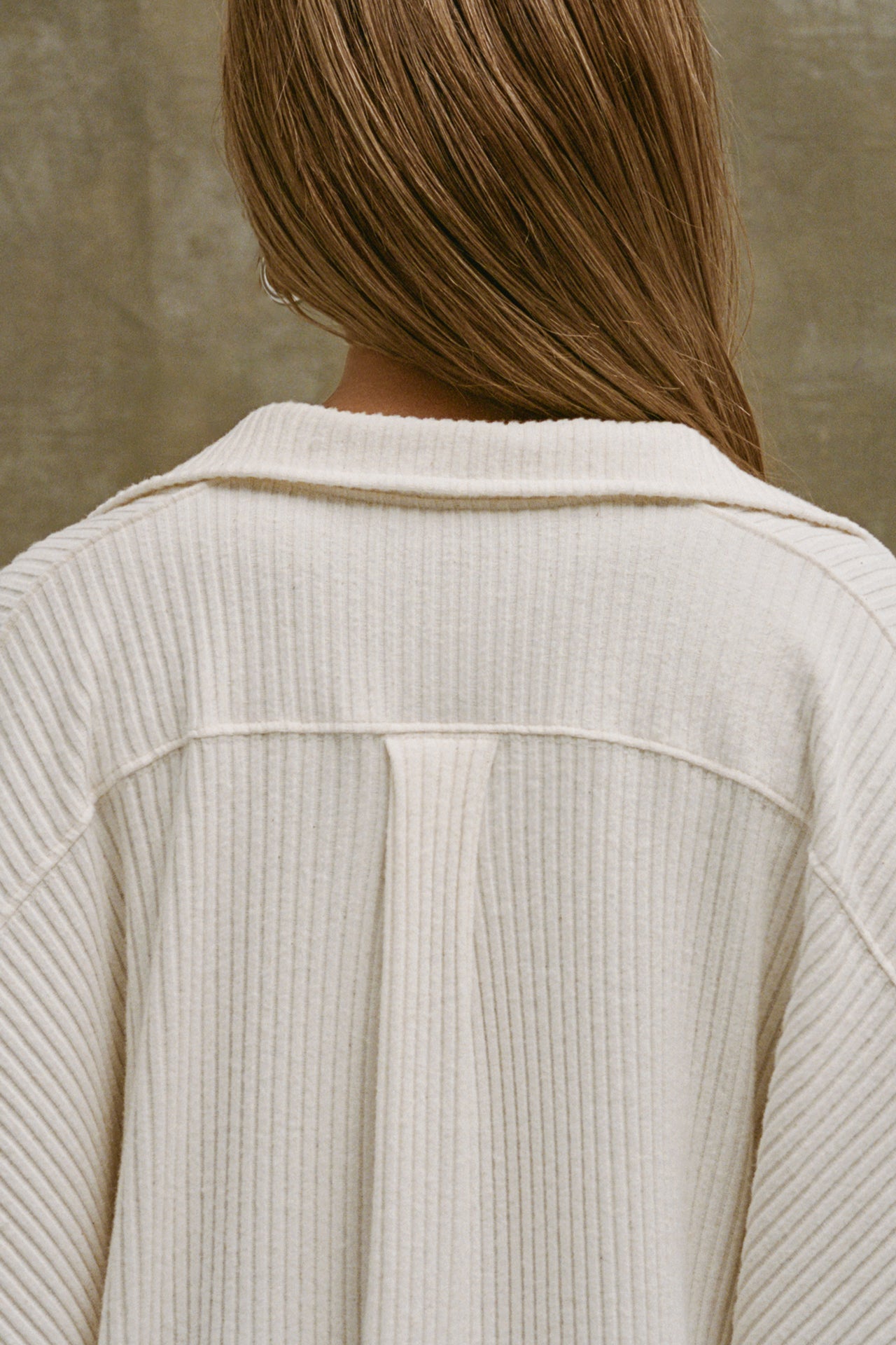Close up back view of model posing in the oversized natural luxe knit Deep V Pullover with a plunging collared neckline, dropped shoulders and back panel details