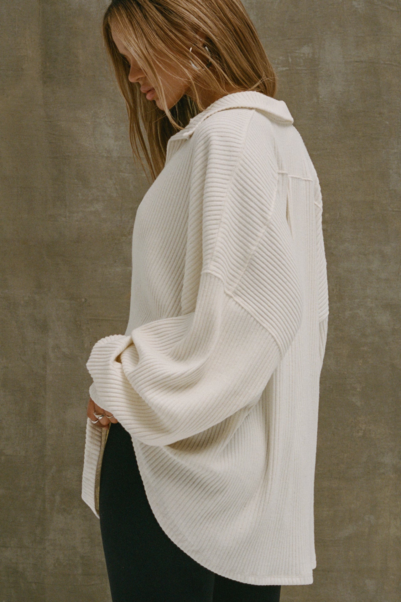 Side view of model posing in the oversized natural luxe knit Deep V Pullover with a plunging collared neckline, dropped shoulders and back panel details