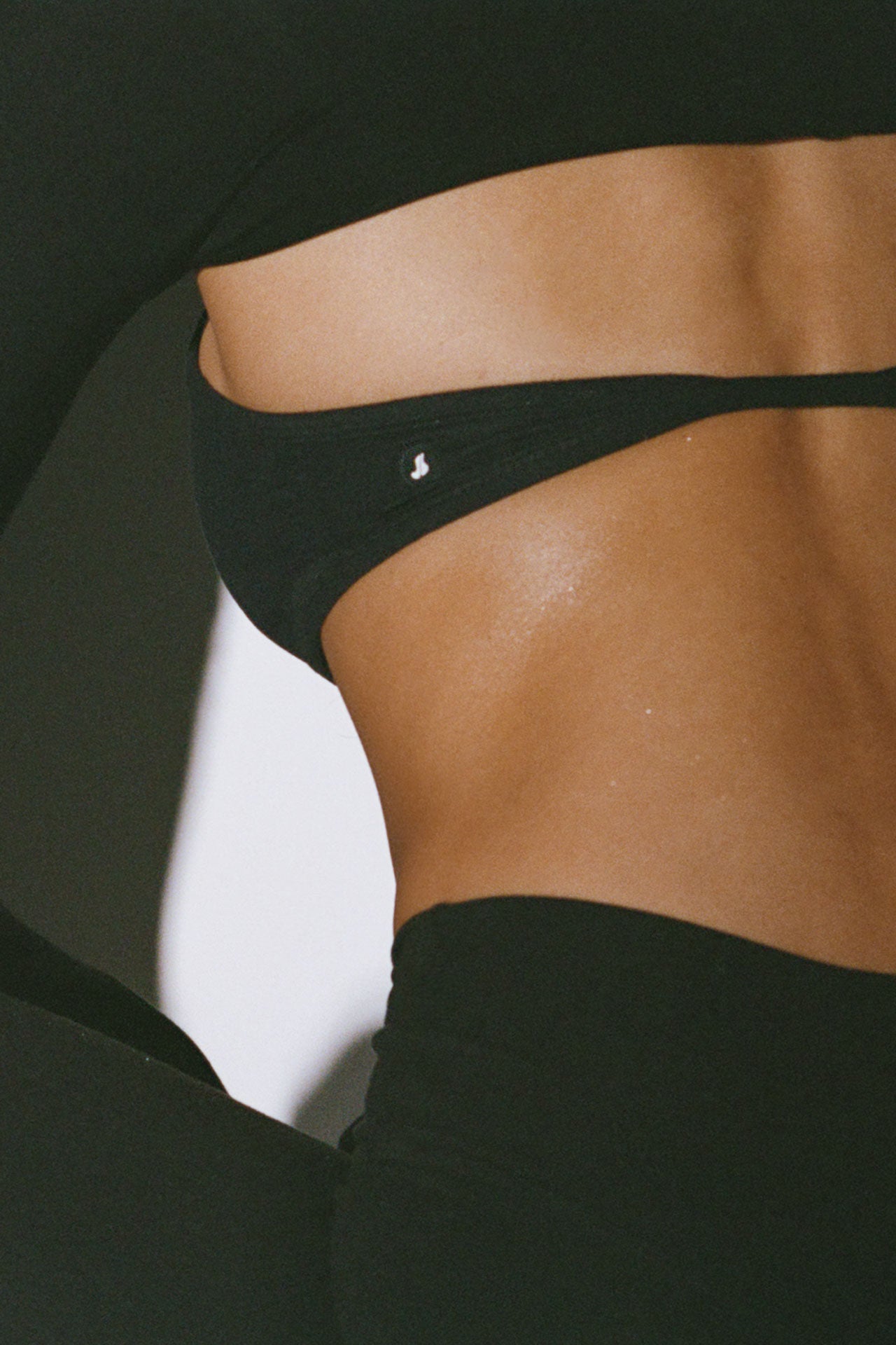 Close up detail back view of model posing in the sueded onyx Halter Scoop Bra top with an adjustable halter neck strap and open back