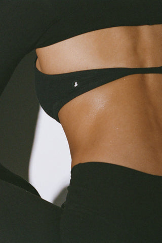 Close up detail back view of model posing in the sueded onyx Halter Scoop Bra top with an adjustable halter neck strap and open back