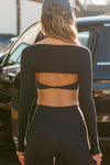 Back view of model posing outside in front of a car in the ultra-cropped and lightweight black modal Shrug bolero cardigan fitted long sleeves
